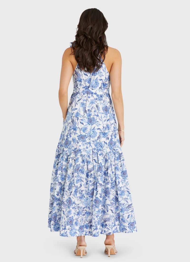 Rear view of a model wearing Aqua Blu Australia Azalea Zoe Dress in blue floral print with halter neckline and maxi skirt