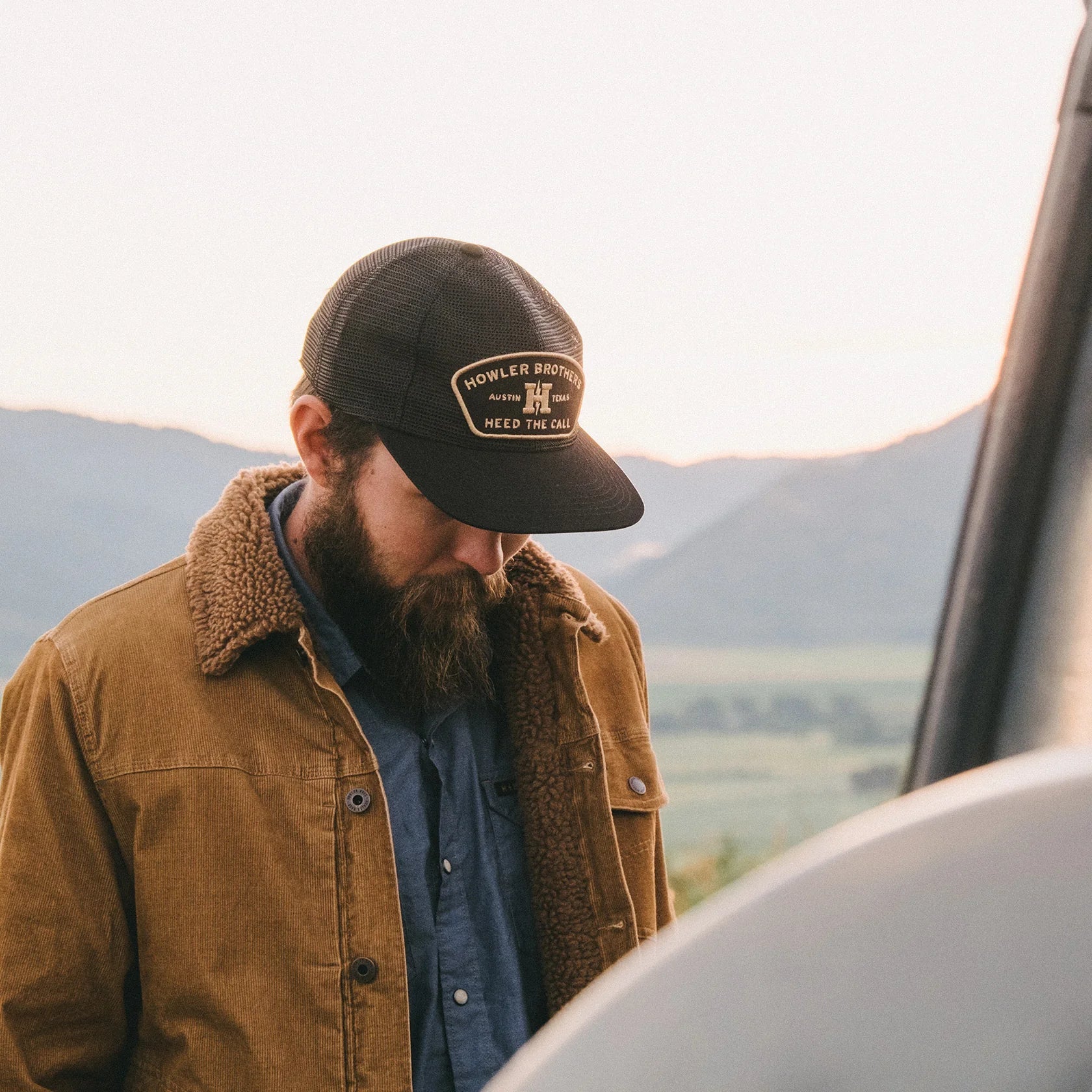 Man wearing a Howler Brothers cap and the Fuzzy Depot Jacket with mountains in the background