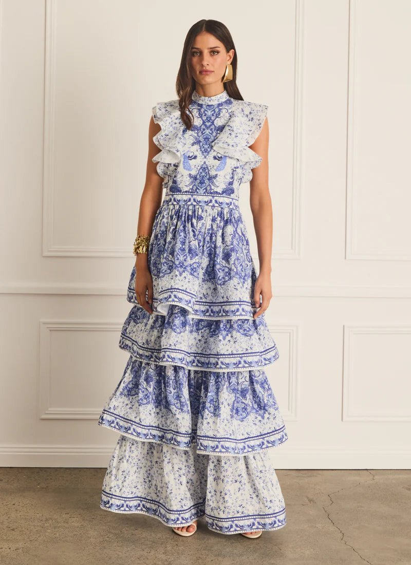 Model wearing the Aqua Blu Willow Lily Maxi Dress in a blue and white floral print, featuring a high neck, tiered skirt, and intricate frill detailing in a luxury French linen and silk blend.