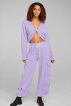 A model wearing a matching lavender two-piece lounge set consisting of a long-sleeve wrap-front crop top and wide-leg cargo pants with side pockets, styled with black boots against a solid gray studio background.