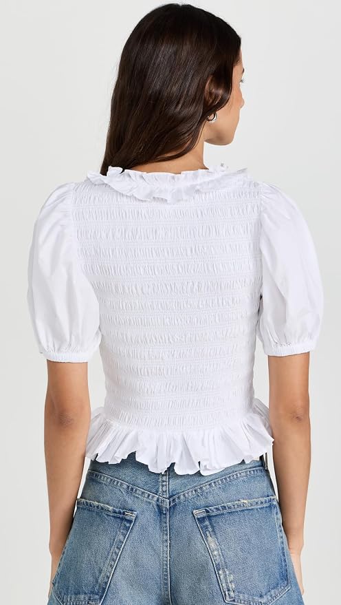 Woman wearing a white blouse with puffed sleeves and blue jeans on a light gray background