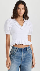 Woman wearing a white blouse with puffed sleeves and blue jeans on a white background