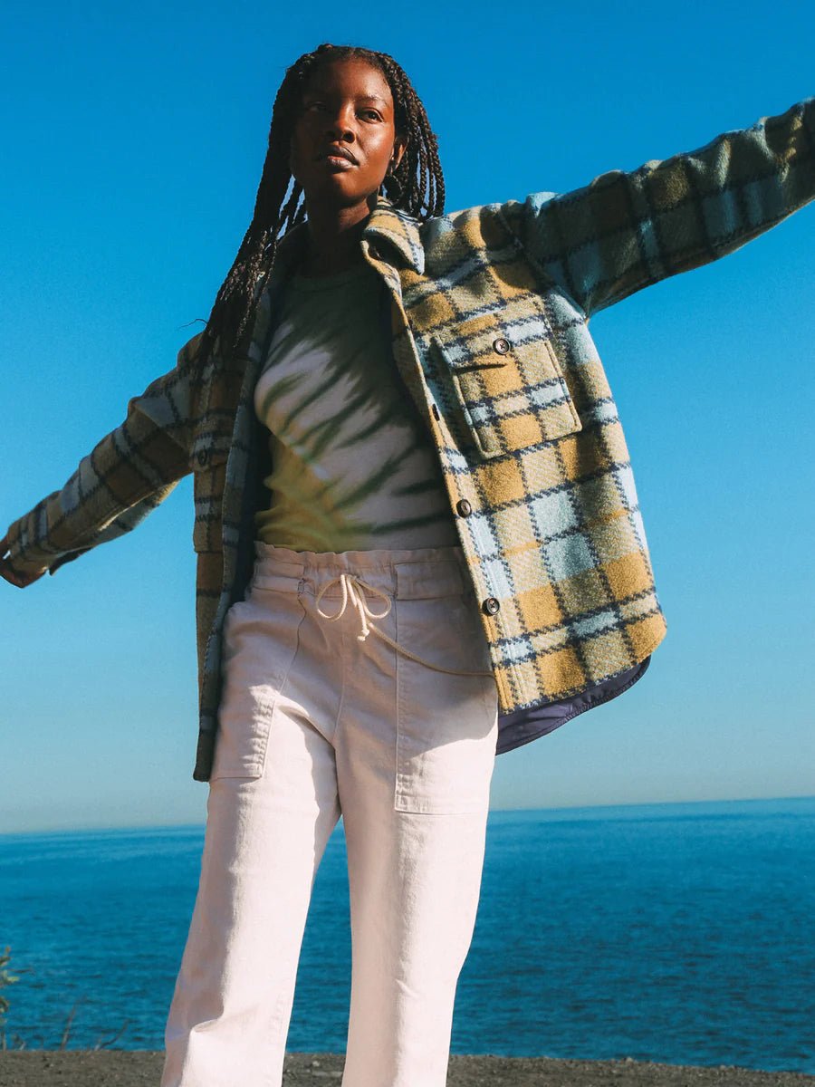 Woman wearing the Electric & Rose Scout Jacket in Indigo Chartreuse plaid against a blue ocean and sky background.