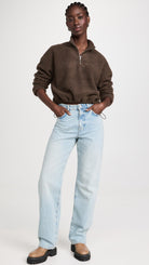 Full view of a model wearing the LNA Sherpa half-zip in brown sherpa showing off the cinachable waist, styled light wash jeans and chunky platform shoes.