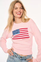 Woman smiling in the LoveShackFancy Ty Flag Sweater, showing the red and blue intarsia American flag and embroidered logo.
