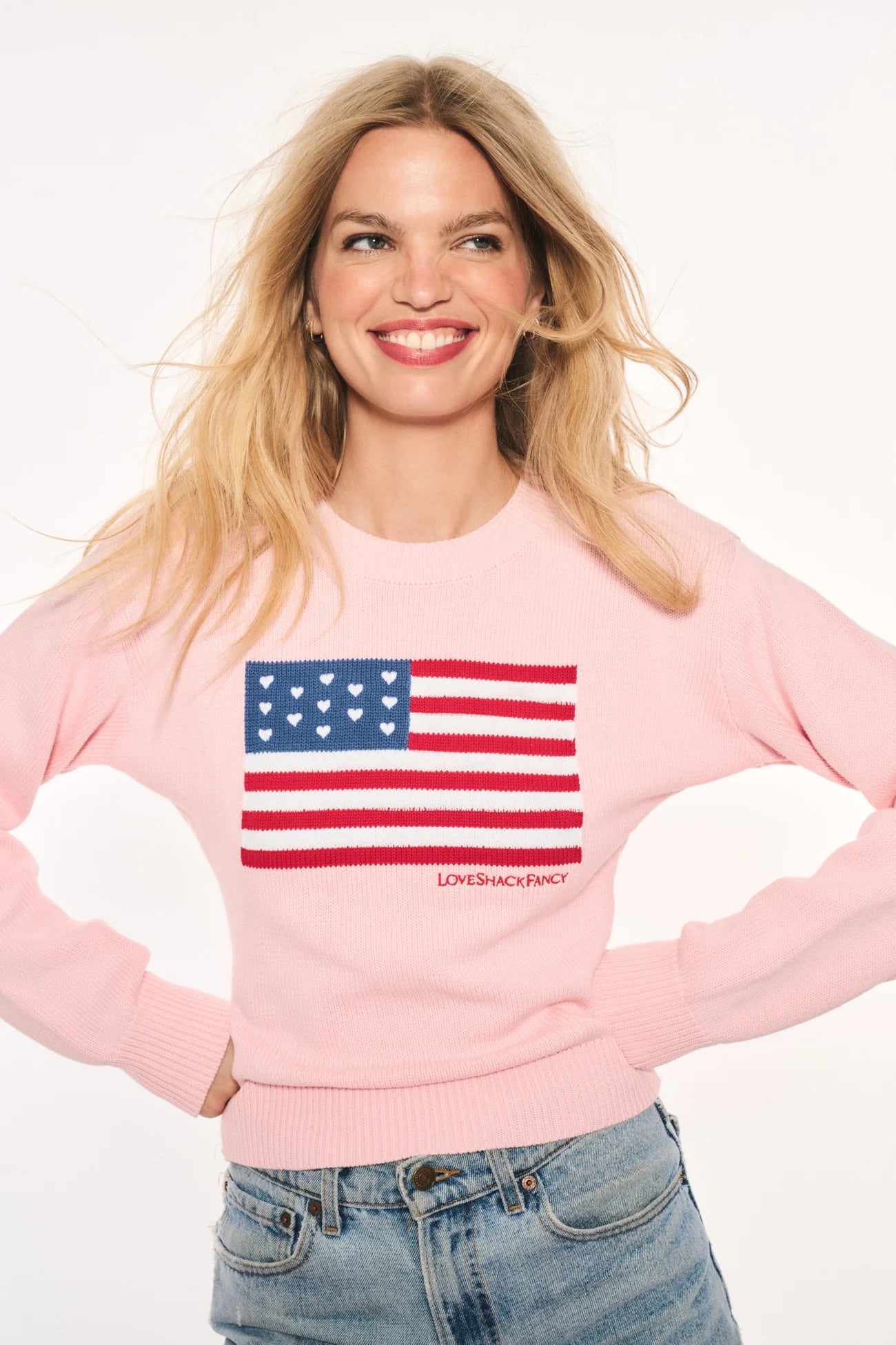 Woman wearing the LoveShackFancy Ty Cotton Flag Pullover in Blushing Liberty pink with an intarsia American flag and heart embroidery.