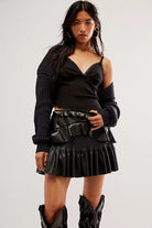 Woman wearing the LoveShackFancy faux leather Eli Skirt styled with knee-high boots on a white background