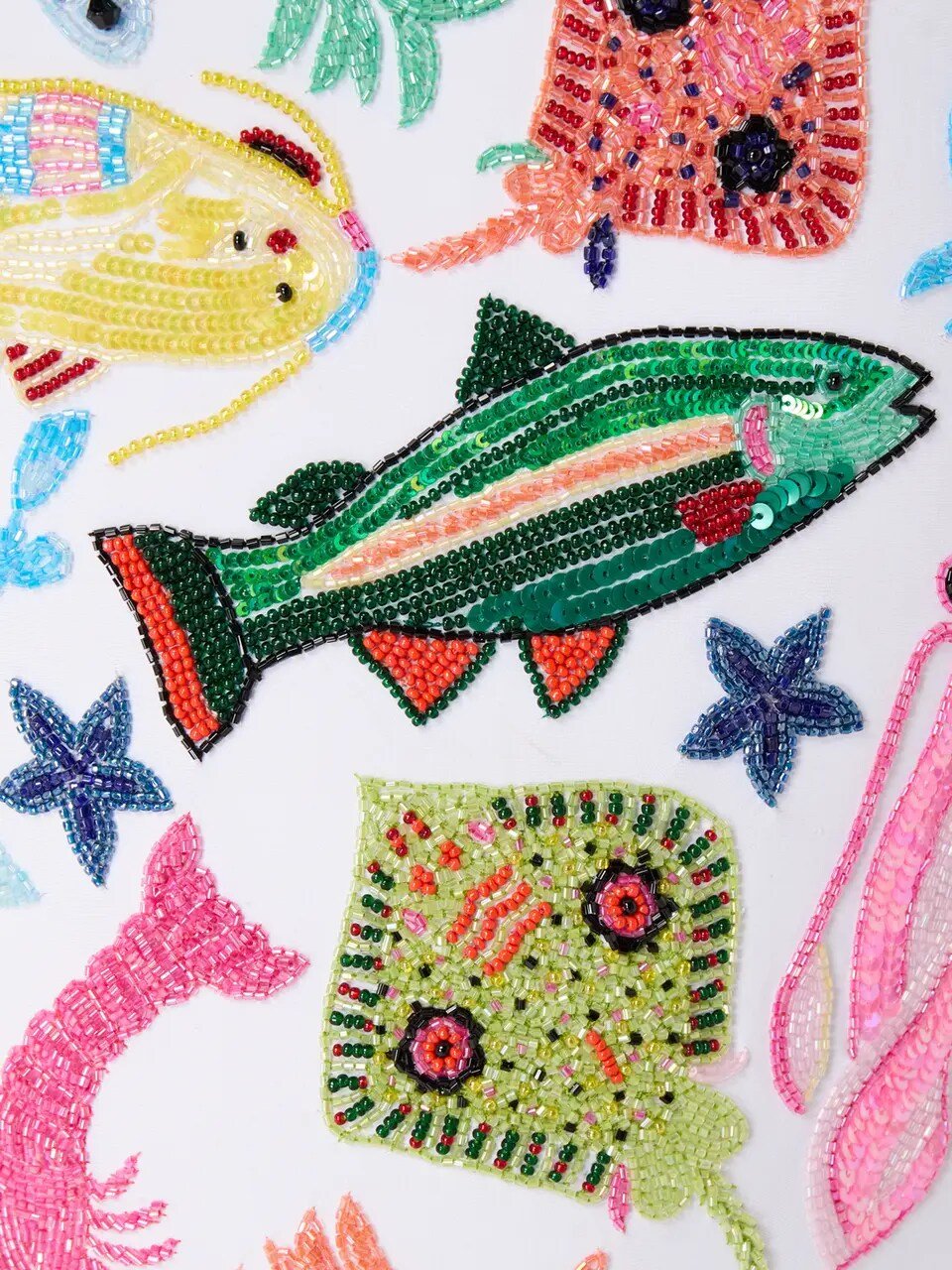 Close-up of the Oceanus Arizona swimsuit embroidery, showing detailed hand-beaded tropical fish, starfish, and coral motifs with shimmering faceted crystals.