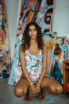 Editorial lifestyle shot of a model wearing the Oceanus Arizona beaded swimsuit in a sunlit art studio, highlighting the vibrant tropical fish embroidery and sparkling crystal details.