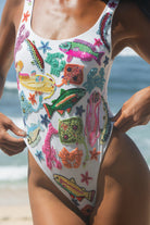 Close-up of a model wearing the white Oceanus Arizona swimsuit, highlighting the intricate hand-beaded tropical fish and coral embroidery with sparkling crystal accents
