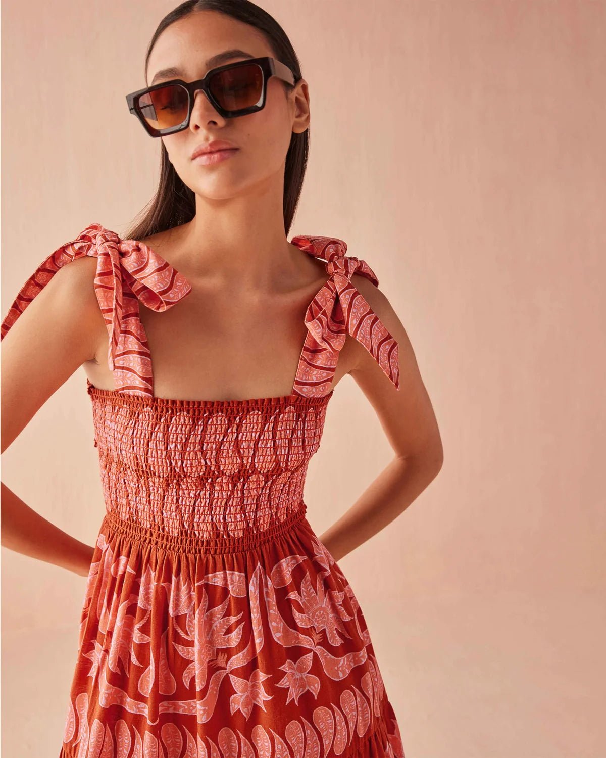 Close-up of the Omika Lana Maxi Dress in Vivi Negroni, showing the smocked bodice and adjustable self-tie shoulder straps in a vibrant orange and pink tropical floral print.