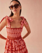 Close-up of the Omika Lana Maxi Dress in Vivi Negroni, showing the smocked bodice and adjustable self-tie shoulder straps in a vibrant orange and pink tropical floral print.