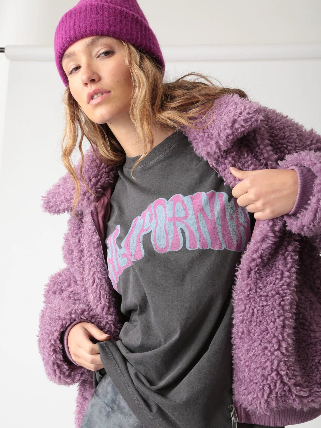 Model wearing a washed black, oversized Electric & Rose Signature Graphic T-Shirt that says CALIFORNIA styled with a sherpa jacket and matching hat.