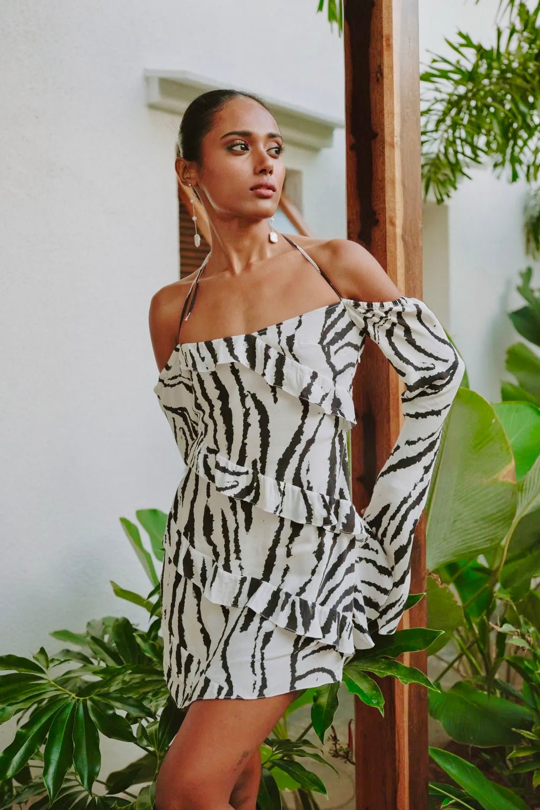 Lifestyle shot of a woman modeling the Summer Away Corsica Mini Dress, a zebra print, long sleeve mini dress with halter neckties.